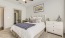 Model bedroom at our apartments for rent in Dallas, TX, featuring carpeted flooring and a view of the bathroom.